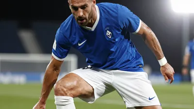 A photorealistic image of an anonymous Málaga CF player, wearing a blue jersey with white shorts and socks, in a tight...