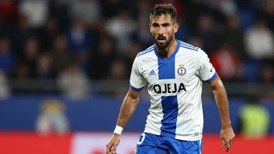 A photorealistic image of an anonymous Málaga CF central defender, aged 25-30, with a rugged build, in a white jersey...