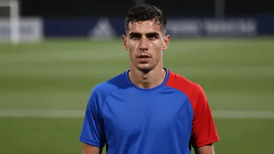 Mid-30s Málaga CF midfielder, athletic build, waist-up in a plain training top split blue left side, red right side...