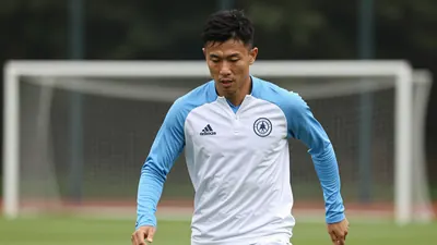 A 28-32 year old athletic midfielder in a solid white and sky blue training kit, mid-stride during a focused warm-up drill