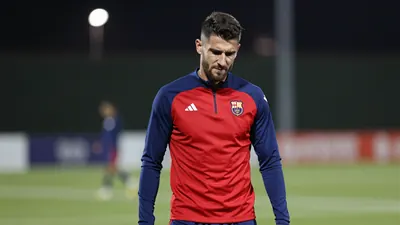 Mid-30s muscular Málaga forward, head tilted, eyes narrowed, shoulders tensed, wearing a plain blue and red training top...