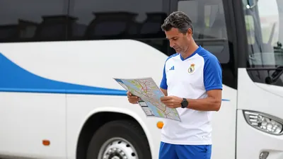 A 35-year-old Málaga CF coach, wearing a white jersey with blue sleeves and a blue short, standing in front of a white...
