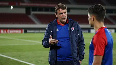 A 35-45 year old, ruggedly built defensive coach, with a weathered complexion, stands on the Estadio La Rosaleda...