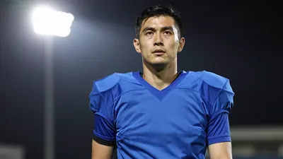 A 30-year-old male football player with a athletic build, wearing a solid blue jersey, photographed with an 85mm f/1.4...
