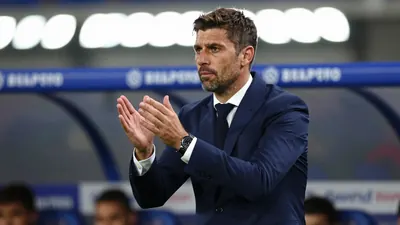 Tight crop of a 30-year-old male football manager in a navy blue suit, mid-gesture on the touchline
