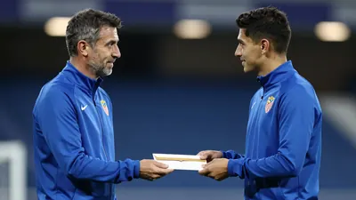 A mid-30s anonymous Málaga CF staff member, waist-up, handing a sealed envelope to a youth coach;
