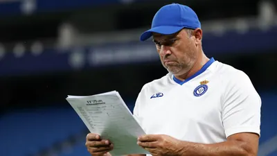 A 35-year-old, 5'9'' (175 cm) male football coach with a strong build, wearing a white Málaga CF jersey with a blue...