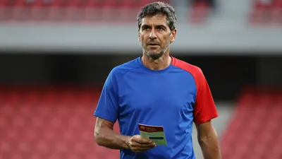 Middle-aged male club official, early 40s, athletic build, waist-up, holding a glossy season-ticket booklet against a...