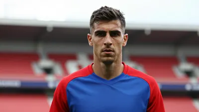 Mid-30s Málaga CF forward, muscular build, intense gaze, head-and-shoulders shot, wearing a plain blue and red training...