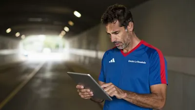 A 35-year-old athletic trainer in a blue and red striped training top, standing on the Estadio La Rosaleda's tunnel wall...