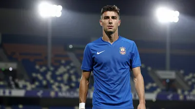 A 25-year-old Málaga CF player, with a lean build, wearing a solid blue kit, photographed with an 85mm f/1.4 lens...