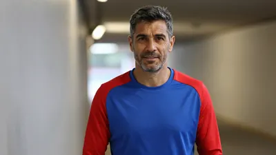 Middle-aged male club official, athletic build, mid-30s, waist-up, wearing a plain, unmarked training top split blue and...
