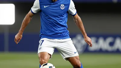 A photorealistic image of a 25-30-year-old, 1.80m tall, athletic build, Málaga CF midfielder, wearing a blue jersey with...