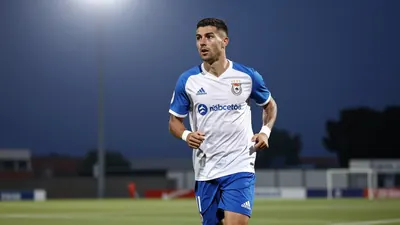 A 25-year-old male Málaga CF player, with a lean build, wearing a blue and white kit, photographed with an 85mm f/1.4...