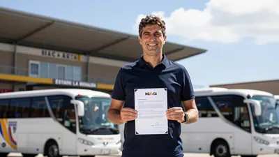 A photo of the Málaga CF coach, Andoni Iraola, holding a transfer document and smiling, with a blurred background of the...