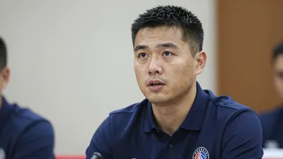 Photorealistic head-and-shoulders shot of a mid-30s male sporting director in a solid navy blue polo shirt, speaking at a...