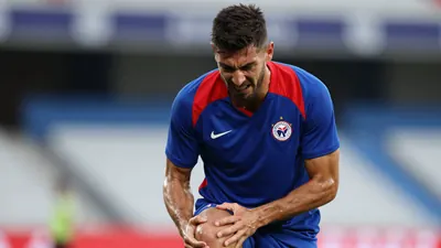 Mid-30s muscular Málaga CF player, head-and-shoulders, grimacing as he clutches his right knee, sweat glistening on a...